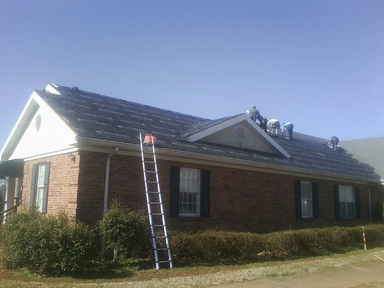Crew tearing shingles off a brick ranch roof with a ladder set — Emergency Roof Repair work by our crew in Allen