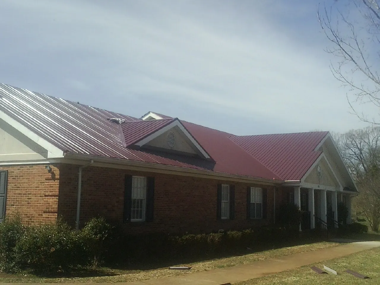Red metal roof with gabled entries on a long brick building, from a Hail Damage Roof Repair job in Allen