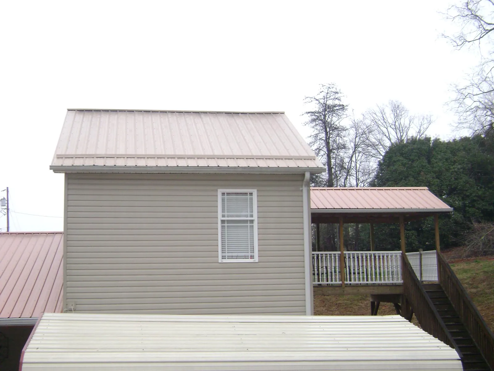 Tan metal roofs on a two story addition and attached porch, from a Roof Replacement job in Allen
